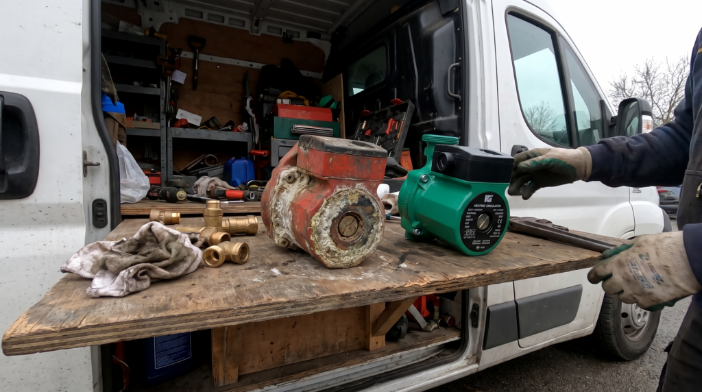 Ancien circulateur de chauffage entartré posé à côté d’un circulateur neuf sur l’établi d’une camionnette d’artisan